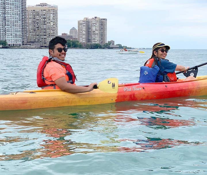two people paddling in a tandem kayak, the front paddler uses an adaptive kayak holder