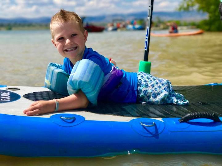 little boy laying on a paddleboard in the water