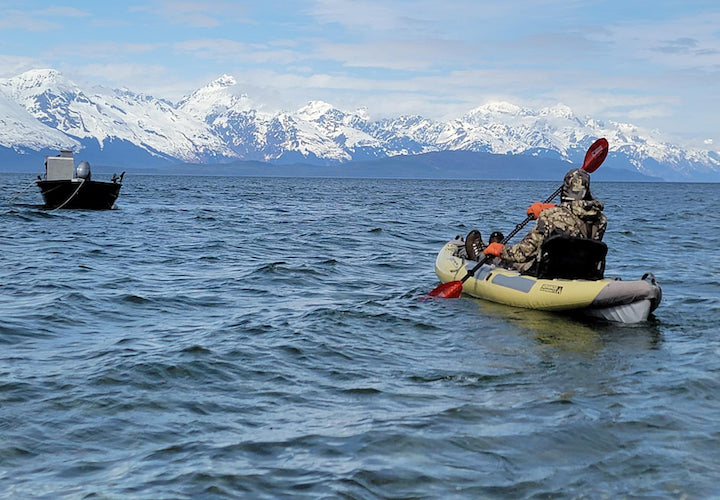 Josiah kayaks out to the anchored boat, mountains in the background
