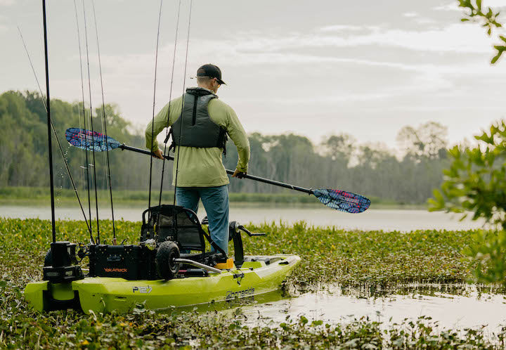 kayak angler standing in his kayak, paddling on a marshy lake