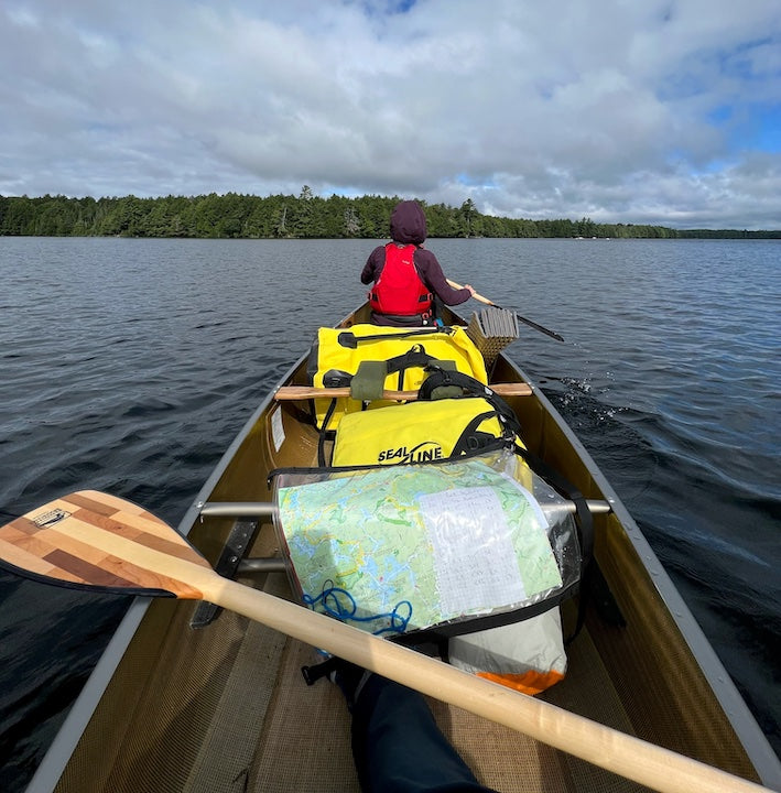 canoeist in the bow; gear and paddle and map in the canoe's middle