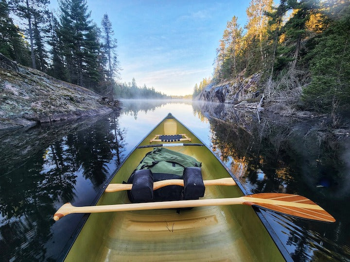 bent shaft canoe paddle laying across a canoe in calm water