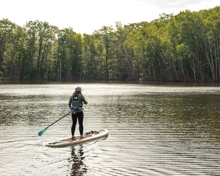 woman paddleboarding on a lake with trees along the shore