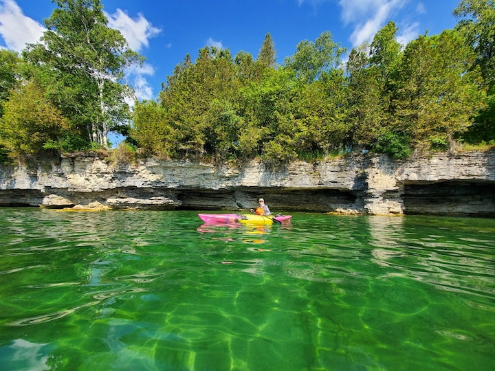 recreational kayaker in beautiful green water with small cliffs and trees behind