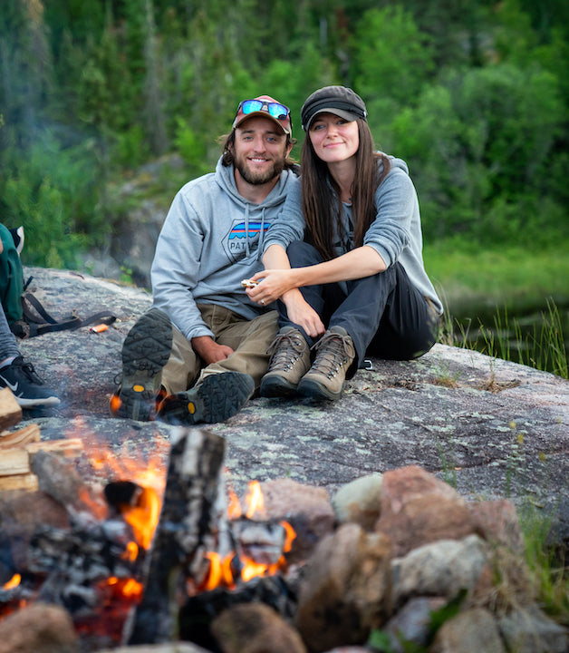 Victor Pilon & Ashley Bredemus sit on a rock next to a campfire