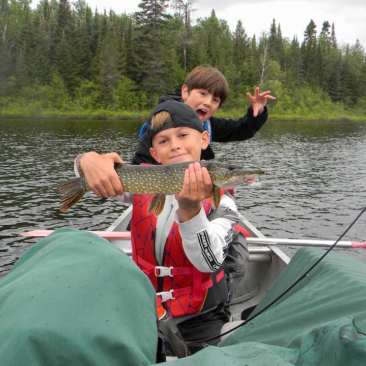 two young boys in a loaded canoe, one holds a nice fish he caught