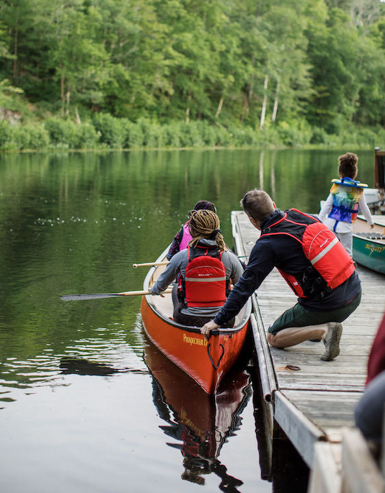 two canoeists ready to launch from a dock, with a bit of help