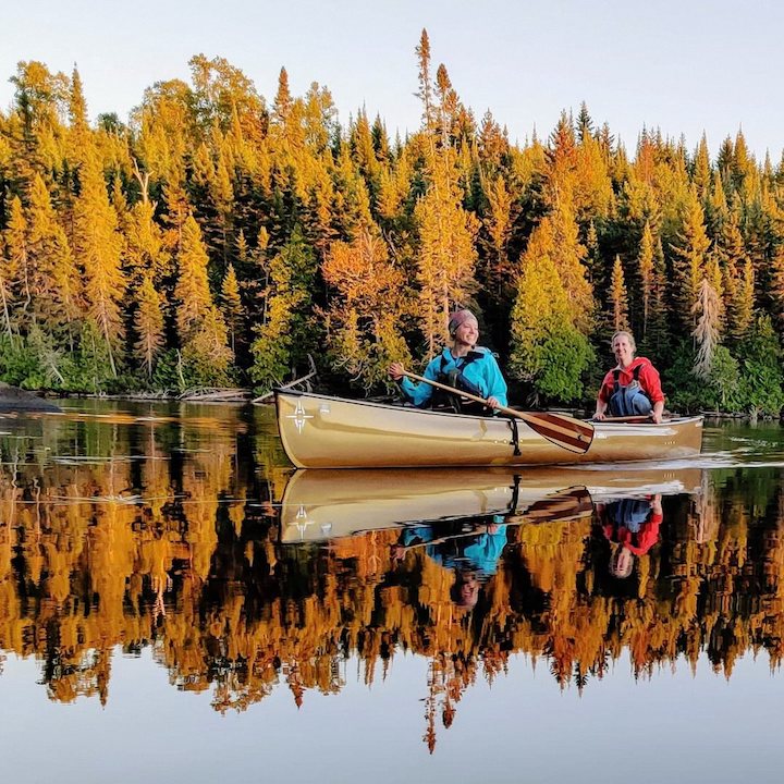 two canoeists on a super calm lake in the fall