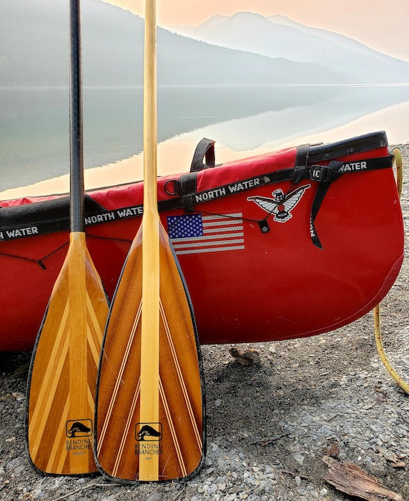 two Bending Branches canoe paddles rest against a red canoe on the shoreline