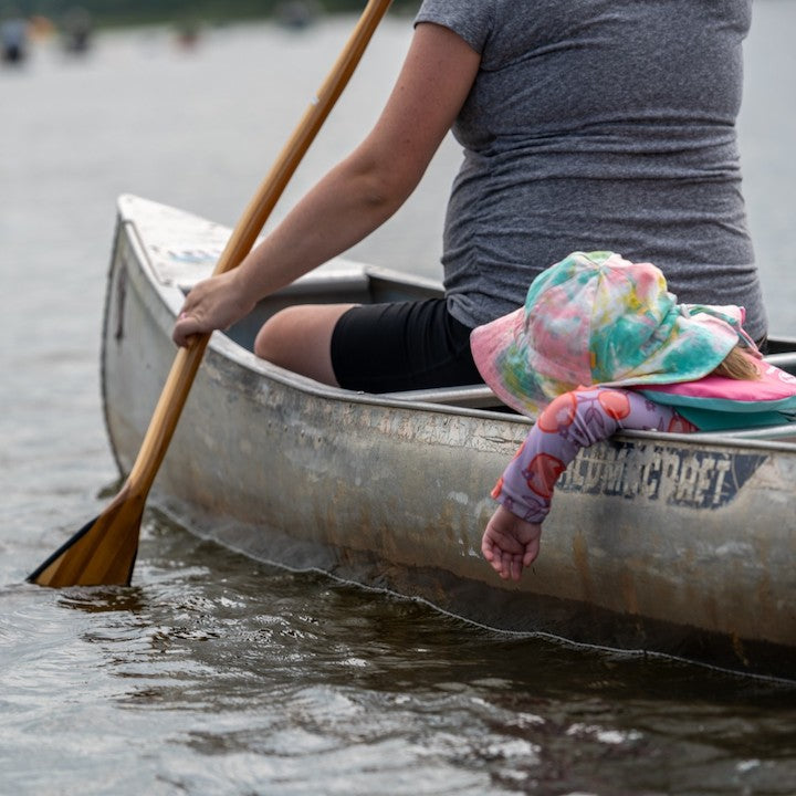 mom paddling an aluminum canoe with toddler behind her in the boat