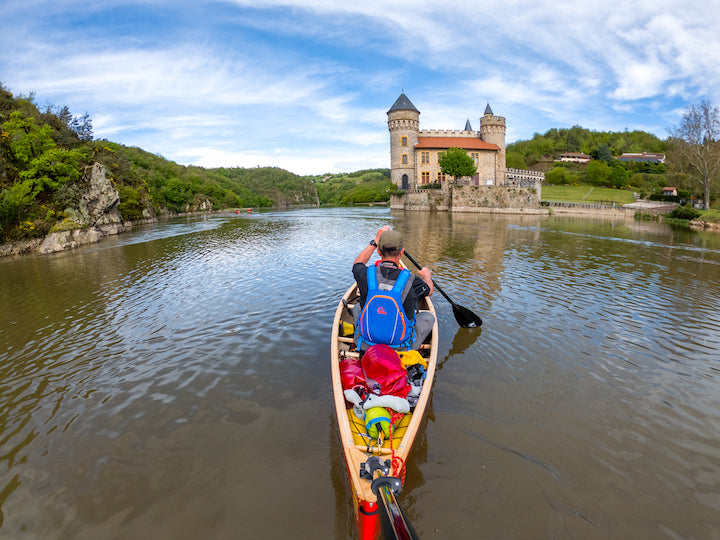 man in a solo canoe using a carbon paddle, castle in the background