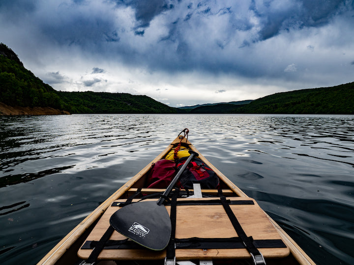 front of a canoe with a carbon canoe paddle; calm lake