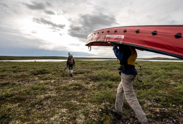 teen boy portages a canoe cross tundra to the next river