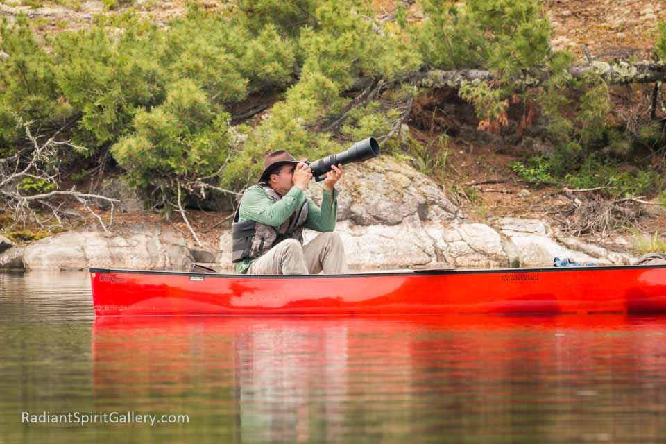 man photographing with a large lens in a red canoe on the lake