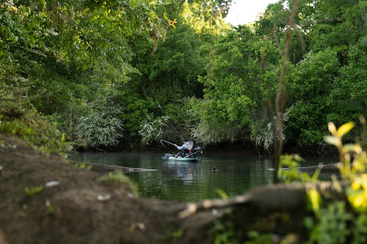 kayak angler fishes in a small cove surrounded by trees