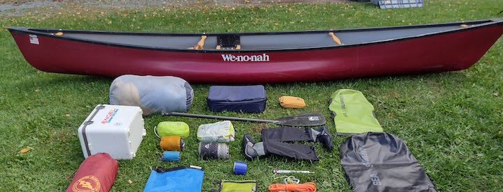red canoe on the ground behind a spread of canoe trip gear