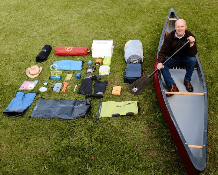 man in canoe on the ground, next to a spread of all his gear