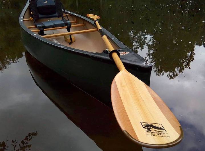 green solo canoe with added chair with backrest, double bladed paddle