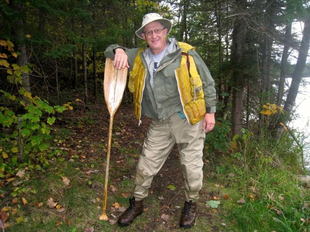 older man with his well-used canoe paddle on shore ready for a canoe trip