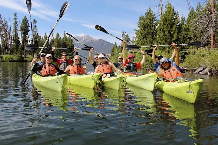 a group of kayakers in yellow kayaks on the water, raising their paddles high