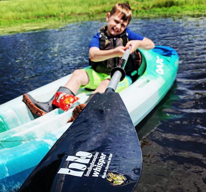 little boy in a kayak on the water with a frog sitting on his kayak paddle blade