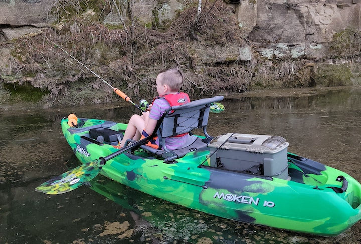 young boy kayak fishes along the shore