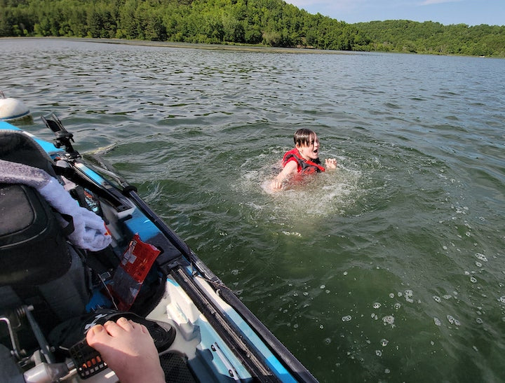 boy swimming next to his dad's fishing kayak