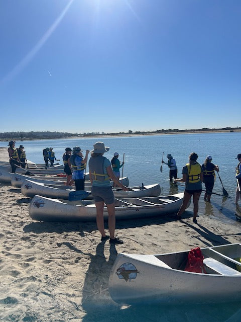 Girl Scouts receive canoe training on shore from adult volunteers