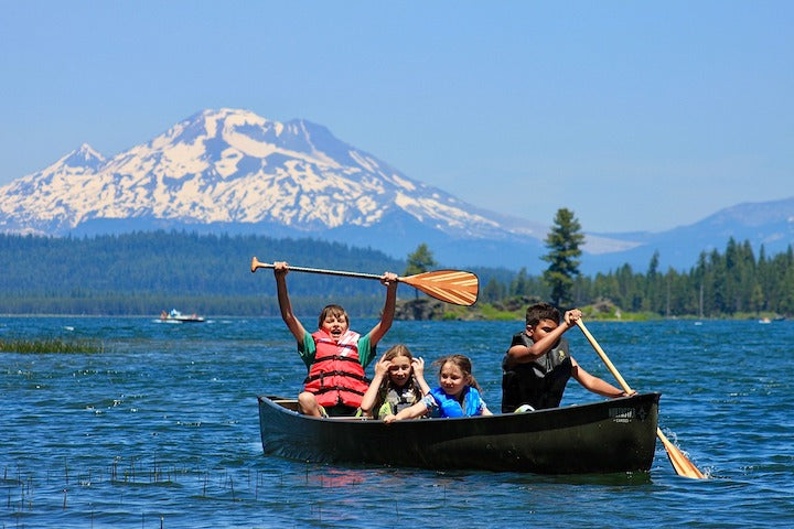 4 children in a canoe together on a mountain lake