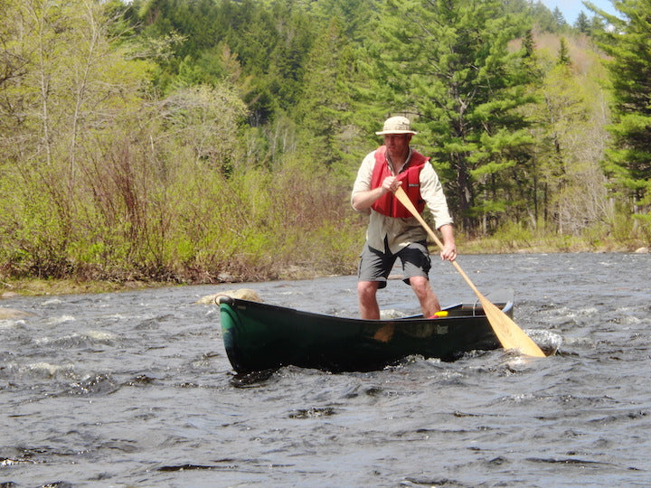 a man standing in his canoe, heading down a river using a Maine Guide Paddle