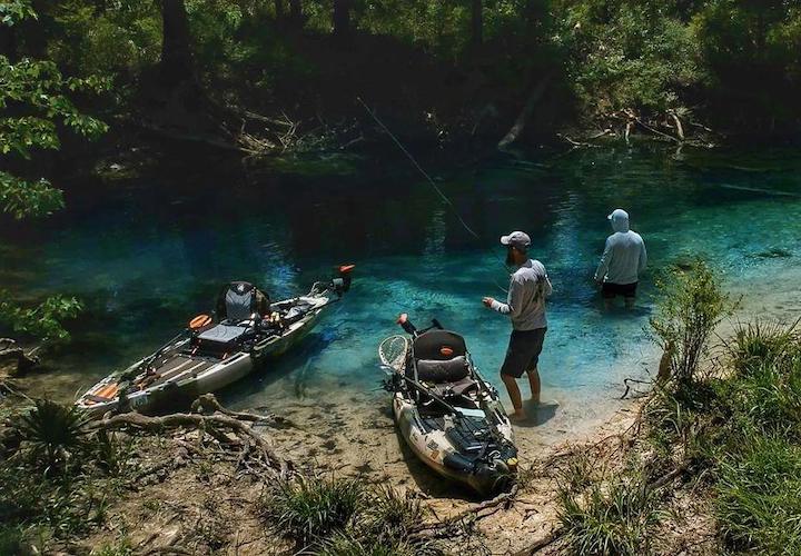 two kayak anglers close to shore alongside their fishing kayaks