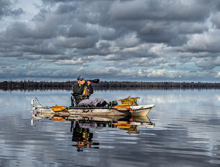 man in a fishing kayak with motor taking a photo