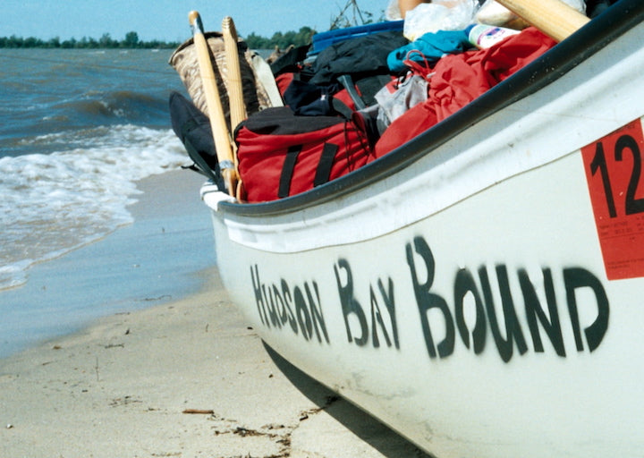 loaded canoe that says "Hudson Bay Bound" on the side, next to the water