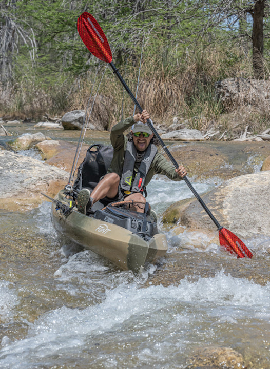 man kayaks through a rapid amid two large boulders