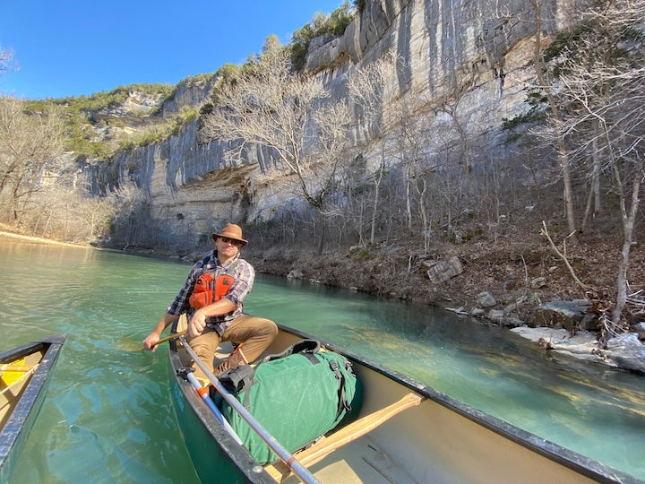 man canoeing with a loaded pack along cliffs