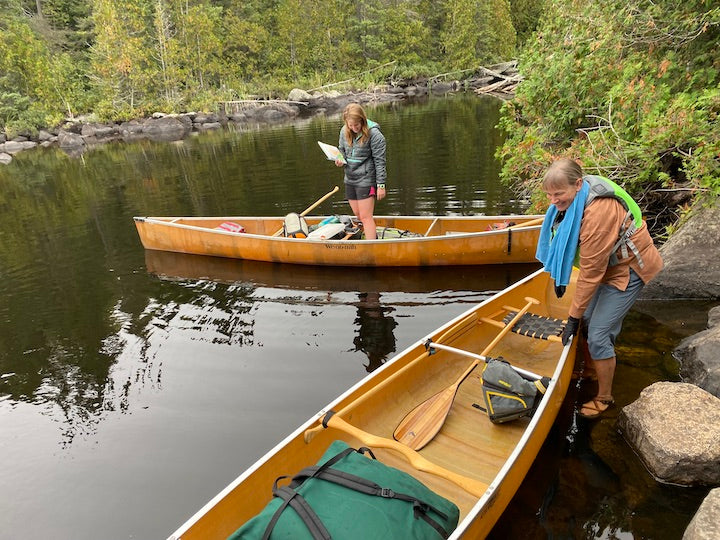 two women each with a canoe, loading up at a portage