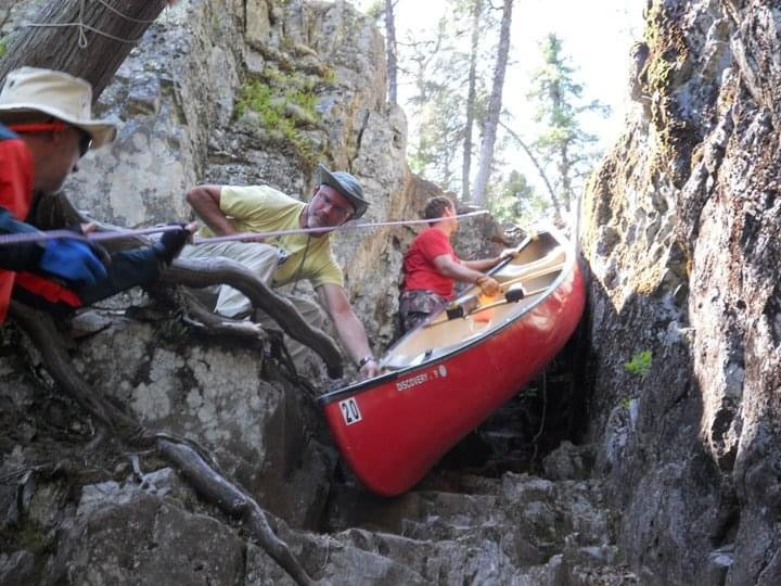 men lowering a canoe down a cliff on a portage