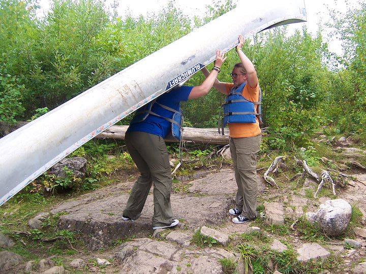 woman bracing canoe for another woman ready to portage