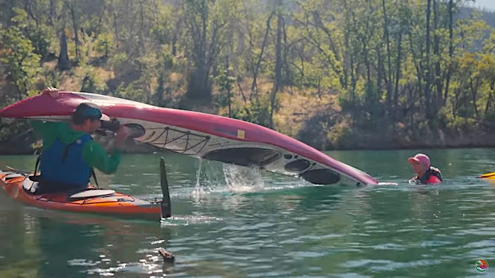 male kayaker emptying water out of capsized kayak, woman in water next to it