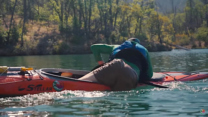 kayaker re-entering his kayak from the water, using a paddle float for stability