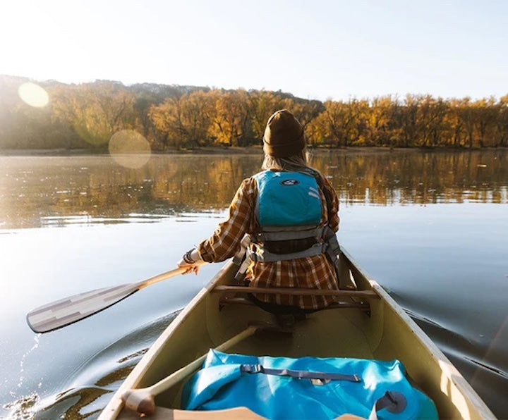 woman sits at the bow of a Grey Duck canoe using a Bending Branches Catalyst paddle on a calm fall day