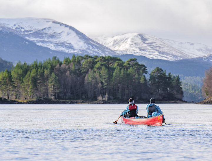 two men canoeing in a red canoe on a Scottish loch with mountains in the background