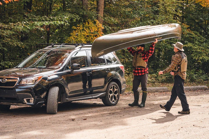 man loads his canoe on top of his small SUV, another man beside him