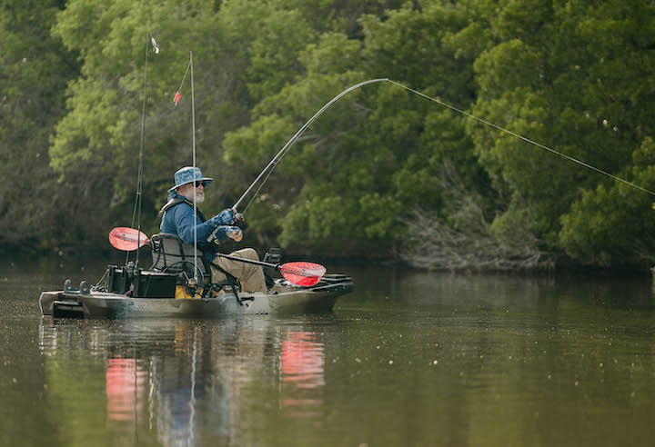 man kayak fishes close to a shoreline