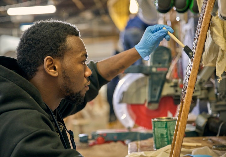 A young man varnishes a canoe seat