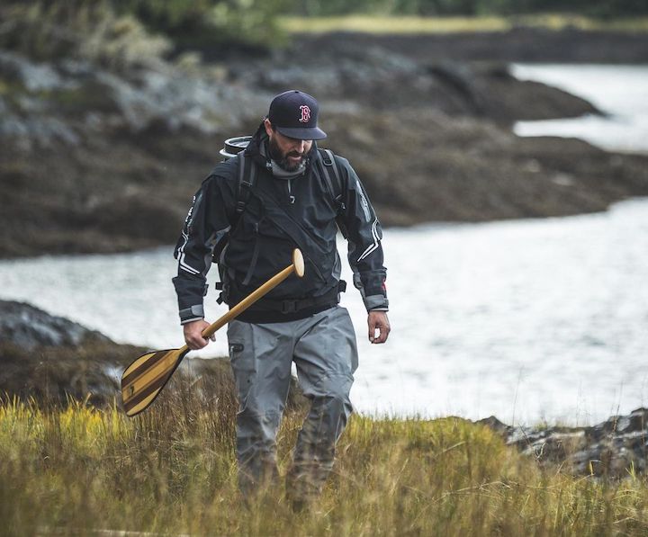 man wearing a drysuit walks along a shoreline with a Bending Branches paddle in his hand