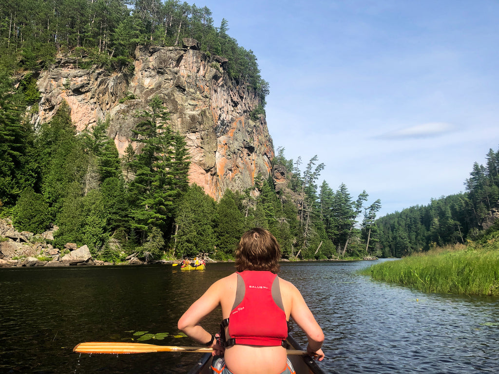 Man is holding a paddling and sitting in a canoe in front of The Natch on the Petawawa River, one of the best canoe trips in Canada.