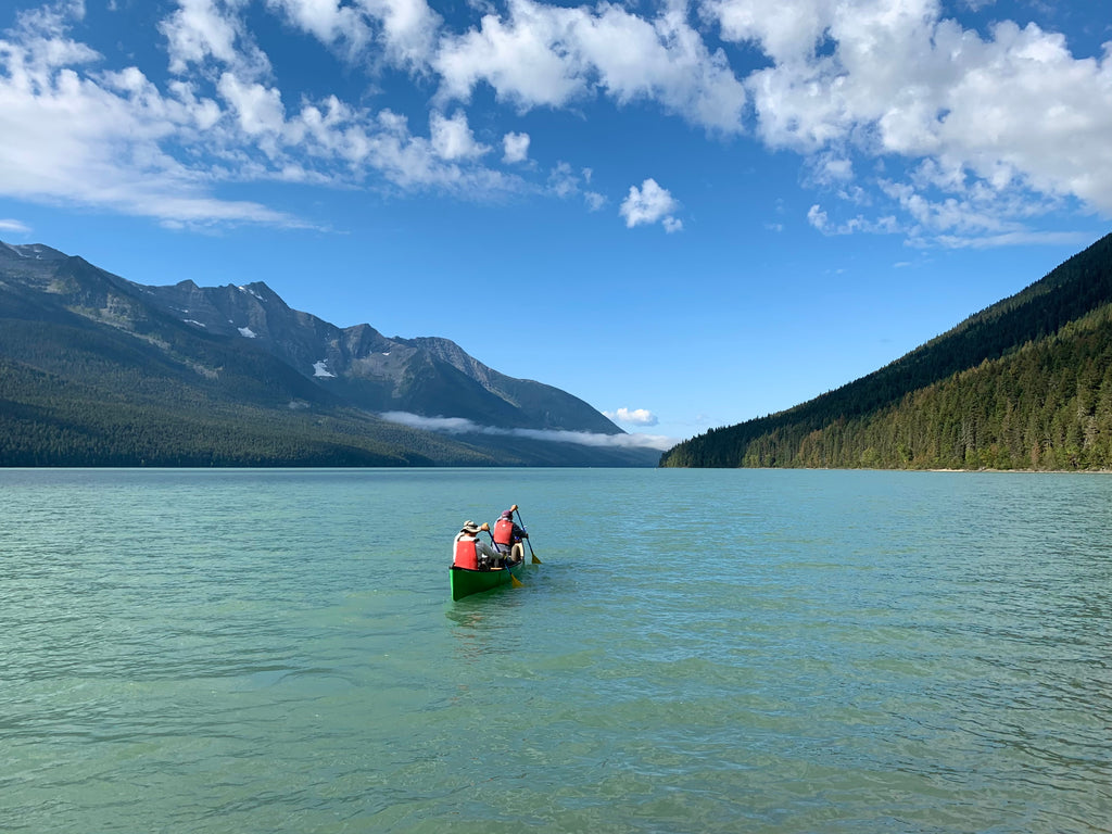 Two people are canoeing on a bright blue lake on the Bowron Lakes Circuit in British Columbia.