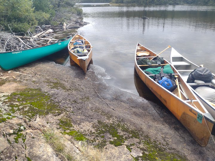 four canoes along shore, loaded down with trip gear