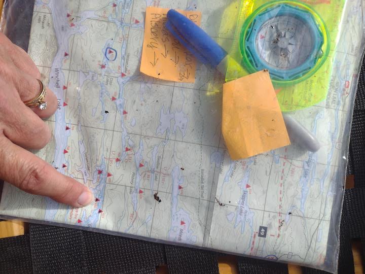 woman's hand pointing to a campsite on a BWCA map, with Sharpie and compass